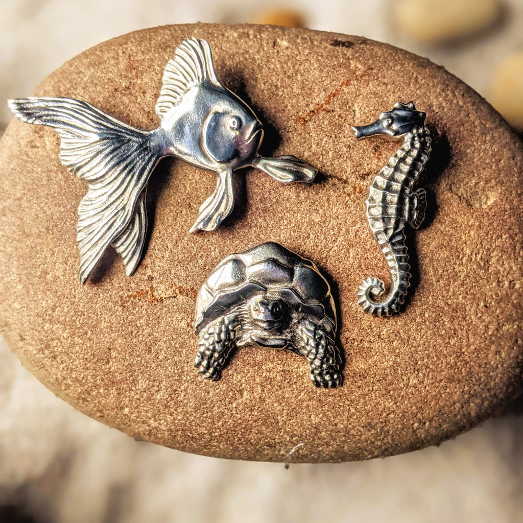 a fish a seahorse and a tortoise in silver on a stone